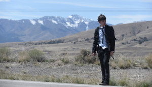 Nick Robinson wearing a suit, tie and backpack on roadside, being charlie movie