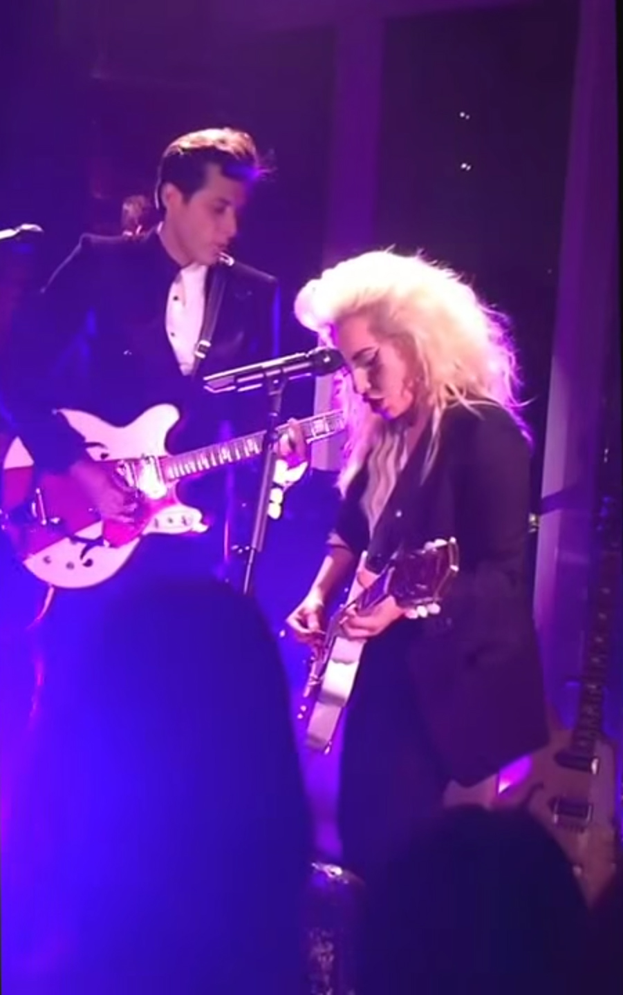 lady gaga and mark ronson playing guitar together on stage in purple light