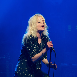 Alison Mosshart of The Kills wearing a star shirt and singing and performing on stage