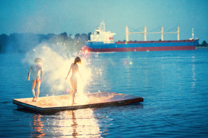 RYAN MCGINLEY, naked woman and man standing in sparklers on the water with a boat in the distance