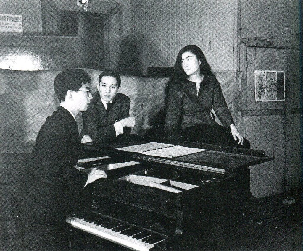 Yoko Ono with Toshi Ichiyanagi (at the piano) and Toshiro Mayuzumi at her Chambers Street loft (1961). Photograph: Minoru Niizuma. Collection of Yoko Ono, New York. © Yoko Ono. Stretching horizontally across the background in this publicity photo for a concert at the Village Gate is one of Ono’s participatory Instruction Paintings.