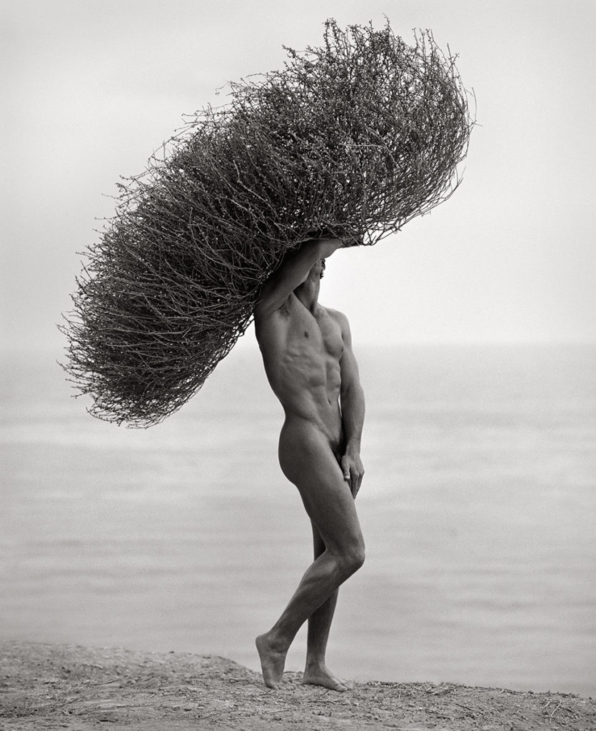Nude male on beach with seaweed crown by Herb Ritts
