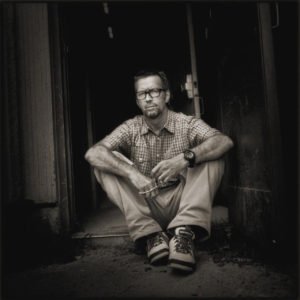 Eric Clapton. Timothy White, 1997. Sitting in a doorway, arms on knees.