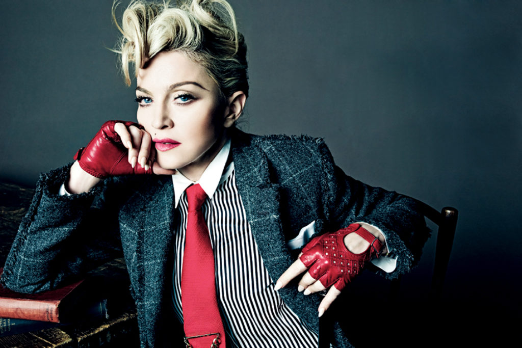 Madonna looking fabulous wearing a glen plaid men's suit, striped shirt, red tie and red driving gloves