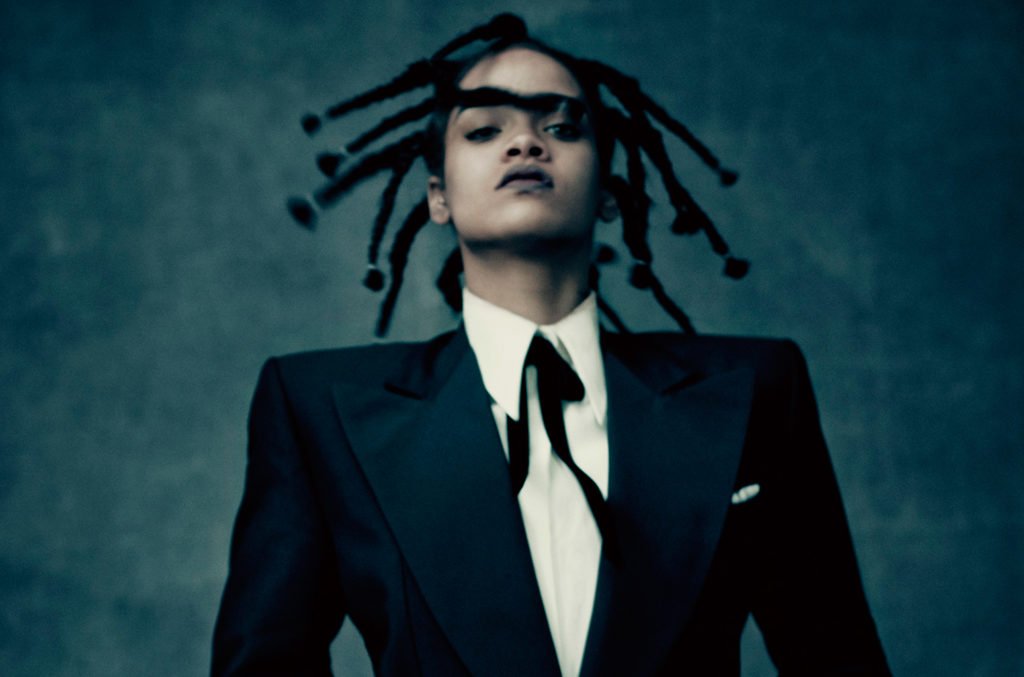 Rhianna looking fierce wearing dreads, a black suit, white shirt and tie