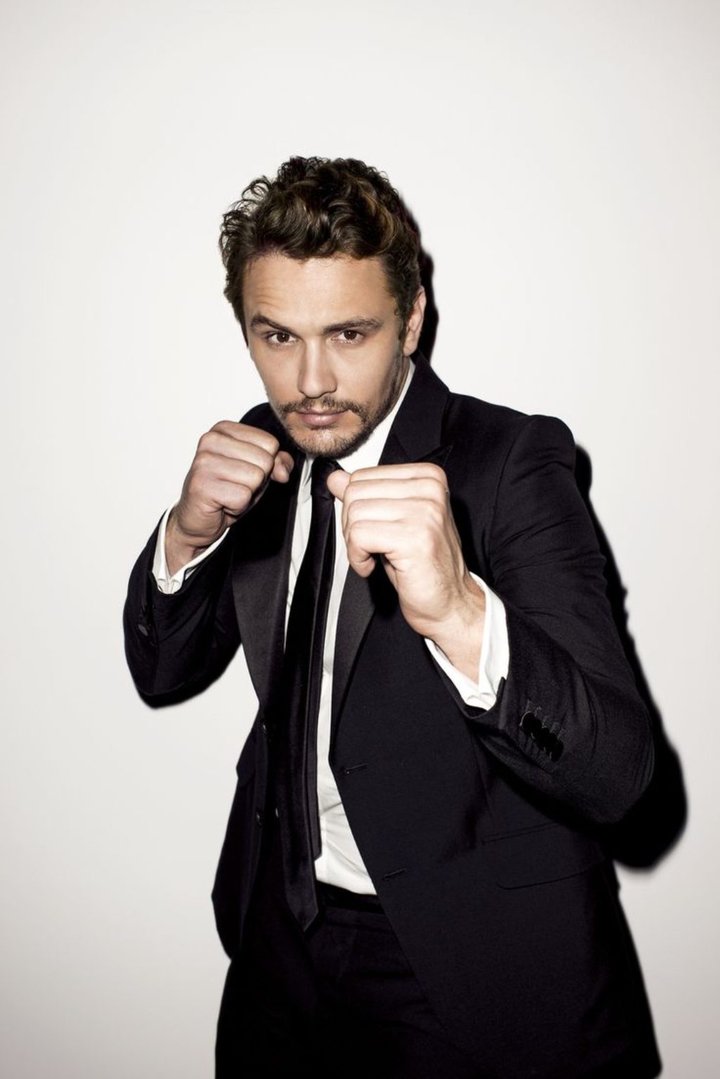 Actor James Franco in a boxing pose wearing a black suit, white shirt and tie