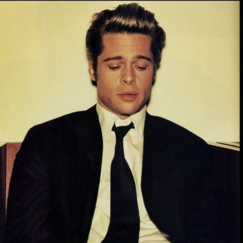 Brad Pitt in his twenties with his signature pout, great hair and beautiful face wearing a black suit, tie and white shirt