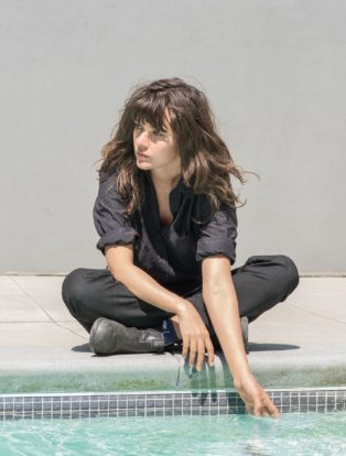 Courtney Barnett sitting by pool hand in water