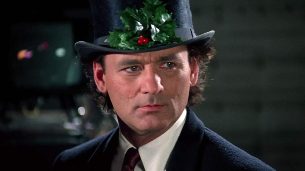 Billy Murray in the film Scrooged wearing a black top hat, holly leaves and red berries