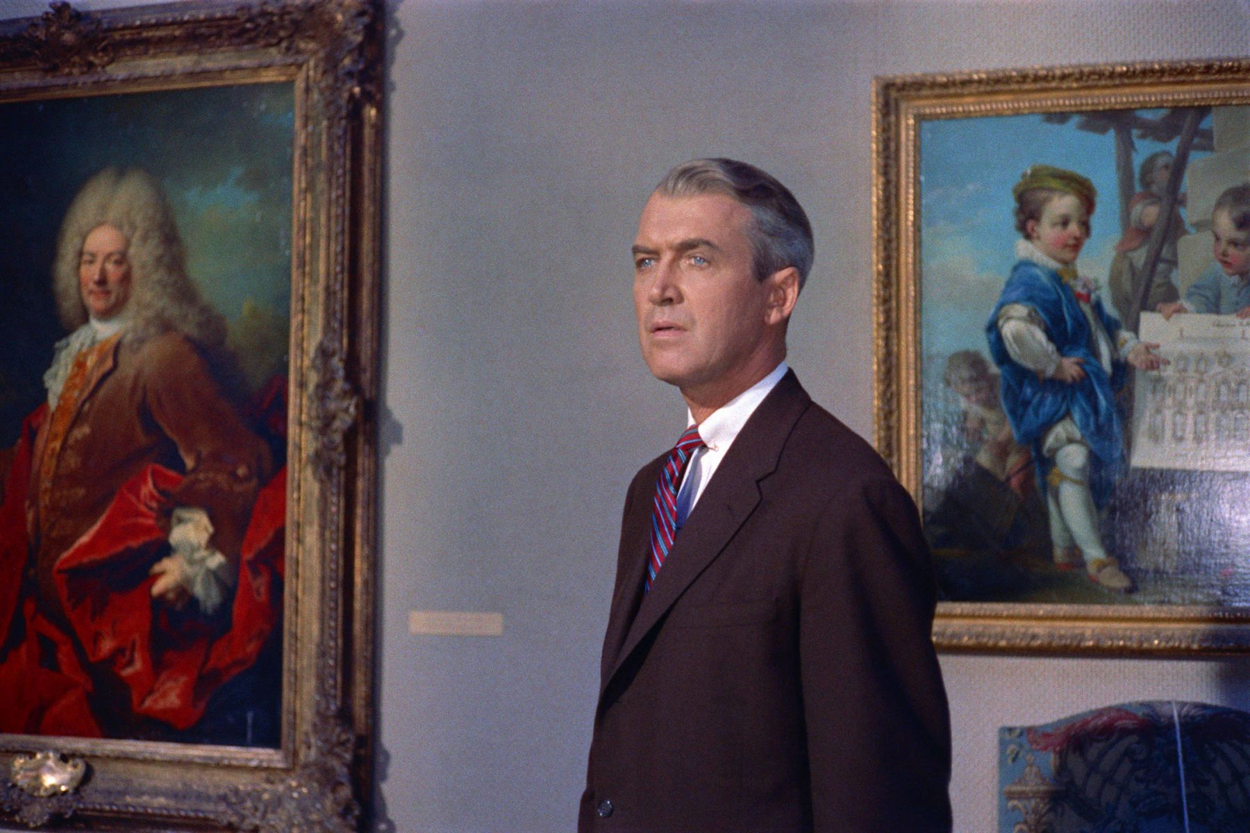 man in a suit stands before two classical paintings