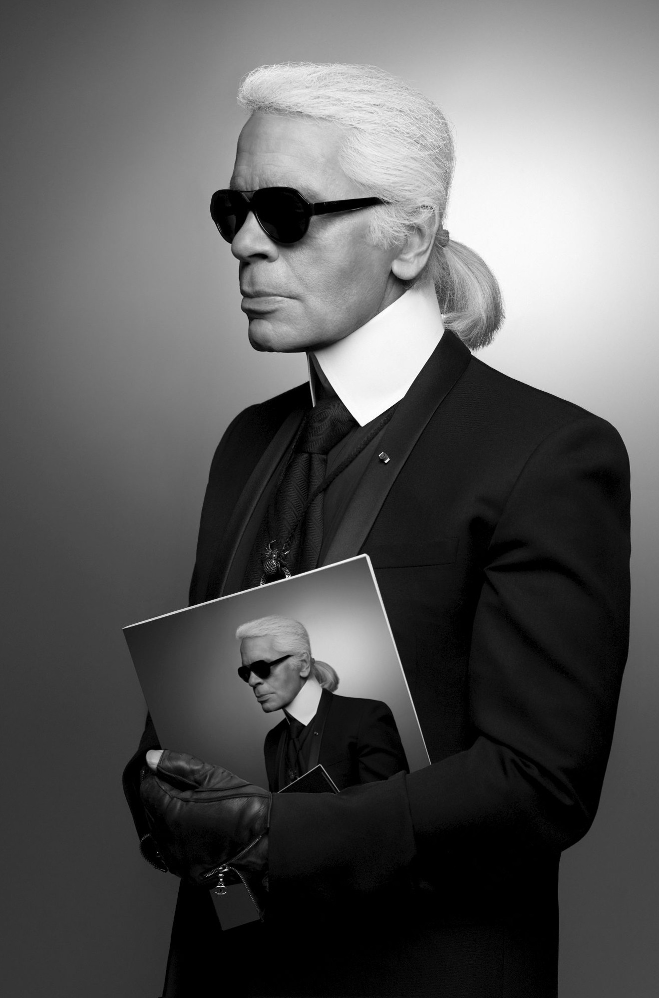 Karl Lagerfeld Holding a Magazine that shows Karl Largerfeld wearing the same outfit he is wearing