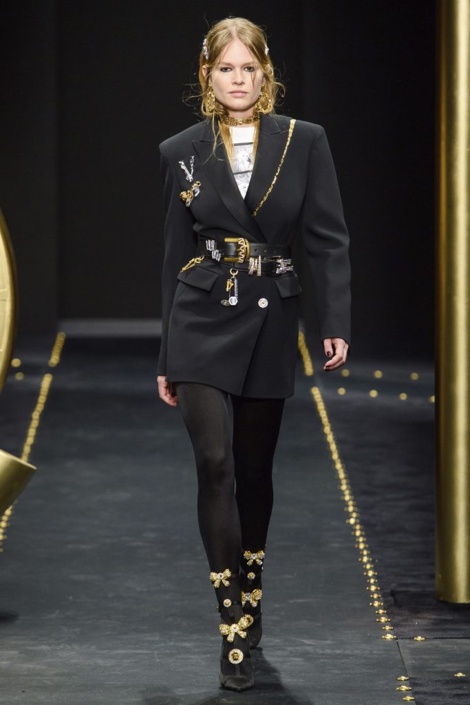 Versace Fall 2019 Runway Show-Model Wearing Black Blazer, Large gold earings, necklace and boots with gold bows