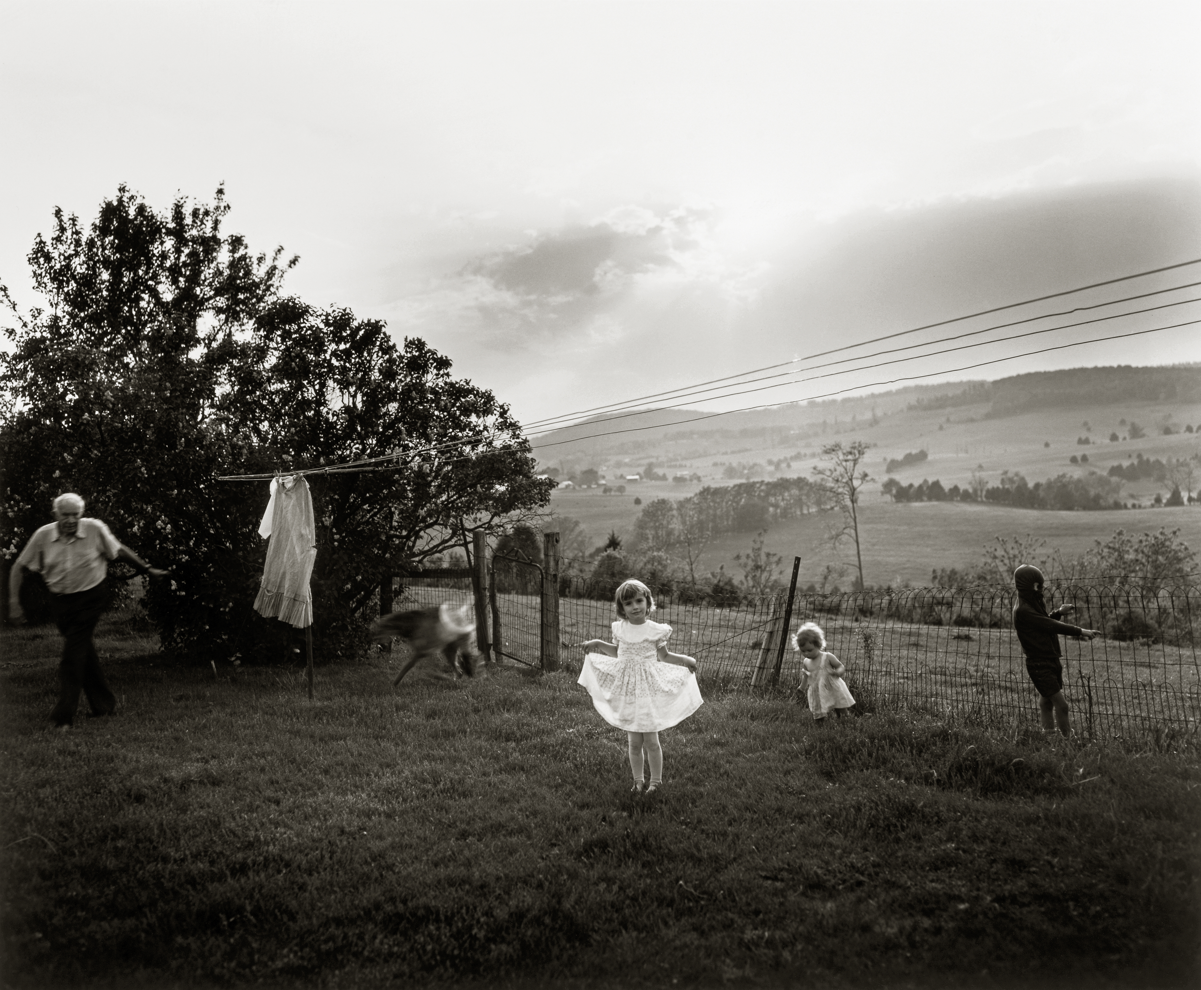 sally mann photograph of a little girl in a white dress, standing in a rural yard