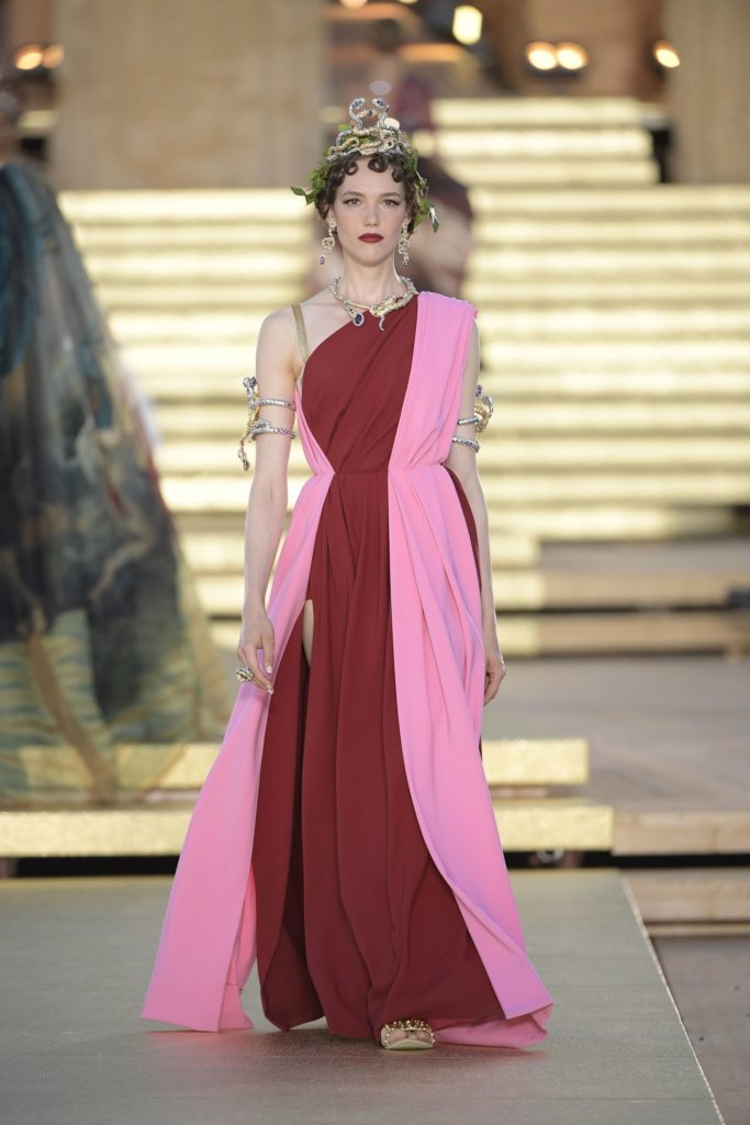 Dolce & Gabbana Runway Show Spring 2019 Model Wearing Red and Pink Roman Robed Dress and Gold and Green Leaf Head Dress