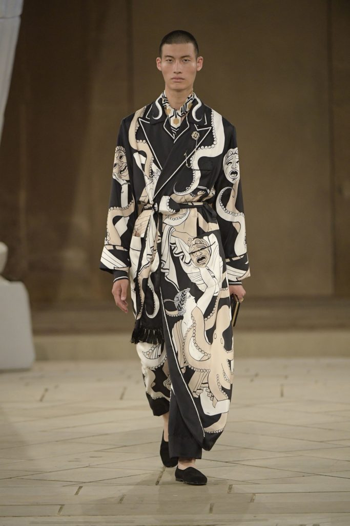 Dolce & Gabbana Runway Show Spring 2019 Male Model Wearing an Ornate Black and White Smoking Jacket with Opera Masks and Art Deco Scarf