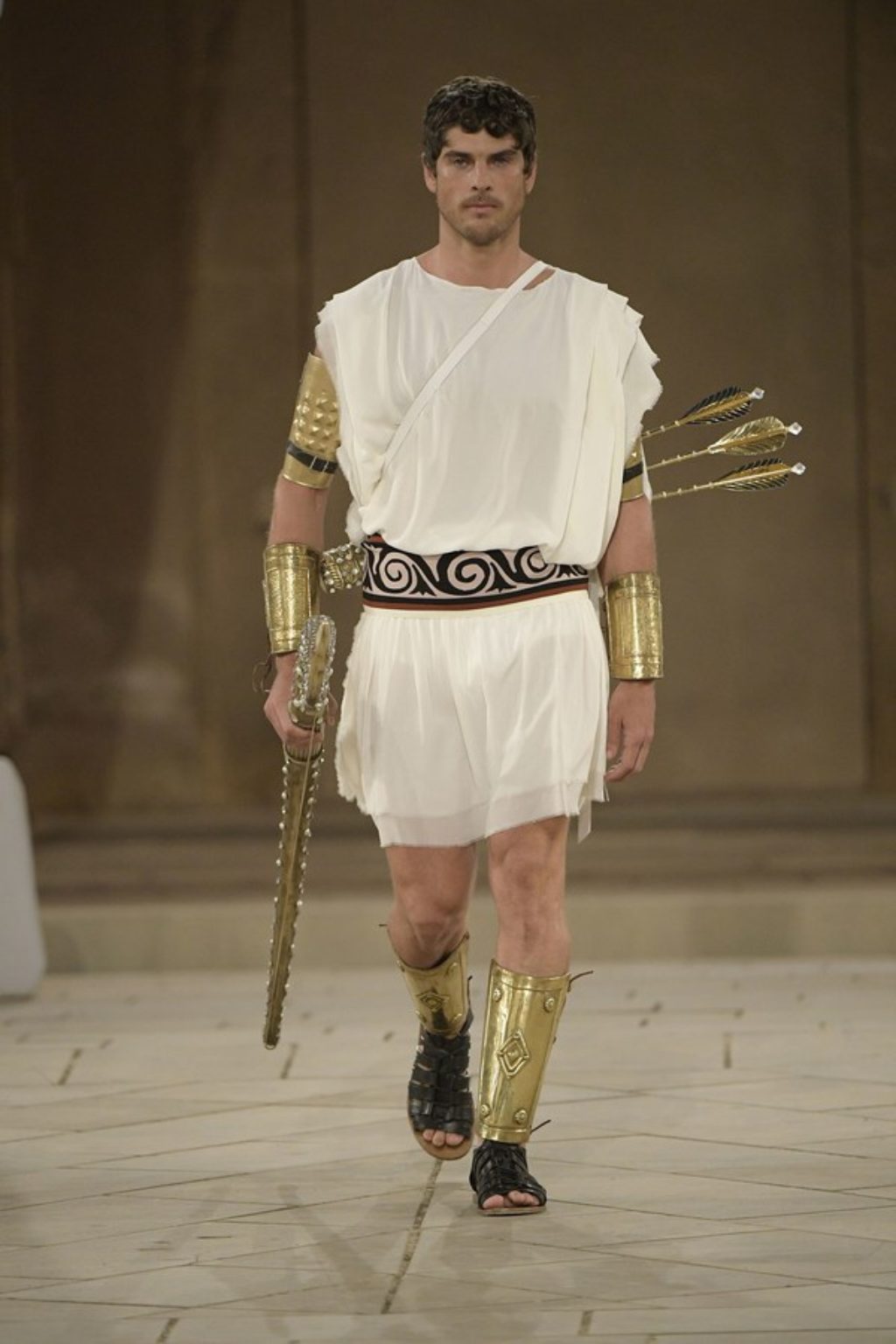Dolce & Gabbana Runway Show Spring 2019 Male Model as a Roman Warrior in Gold Arm and Leg Armor carrying a gold bow and arrows