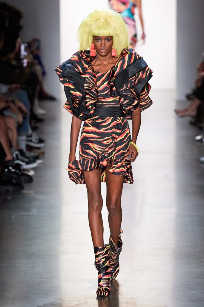 Jeremy Scott Runway SS 2020 Model wearing oversized yellow wig and yellow-black and orange zebra striped ruffled mini dress and matching boots