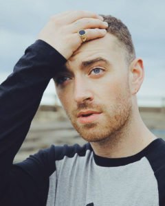 Sam Smith Holding his hand to his head wearing a baseball shirt with navy sleeves and blue sleeves
