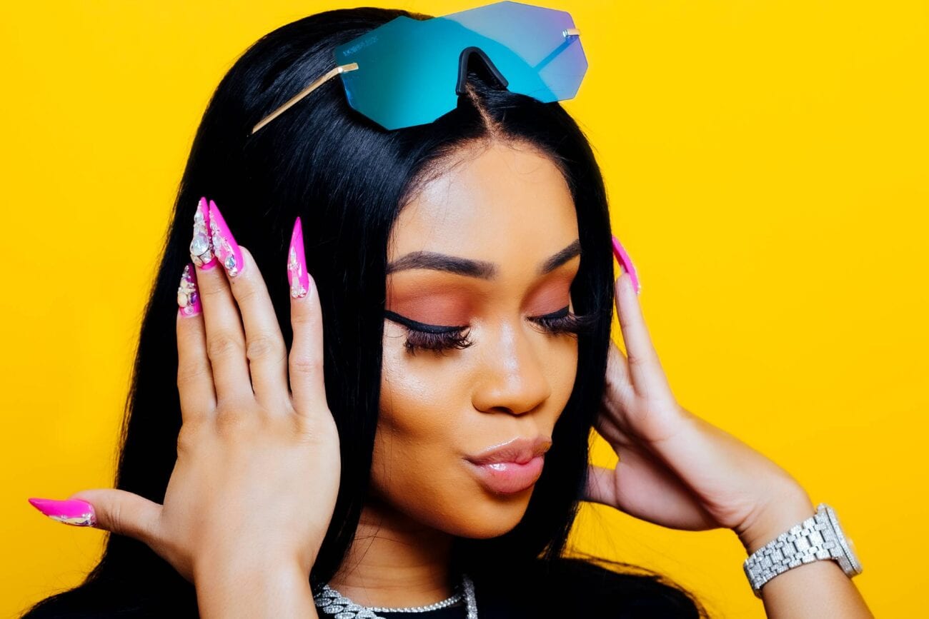 Saweetie with eyes closed and blue shades on her head against a yellow background