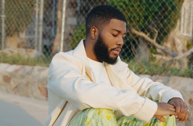 Khalid in white jacket sitting next to chain linked fence