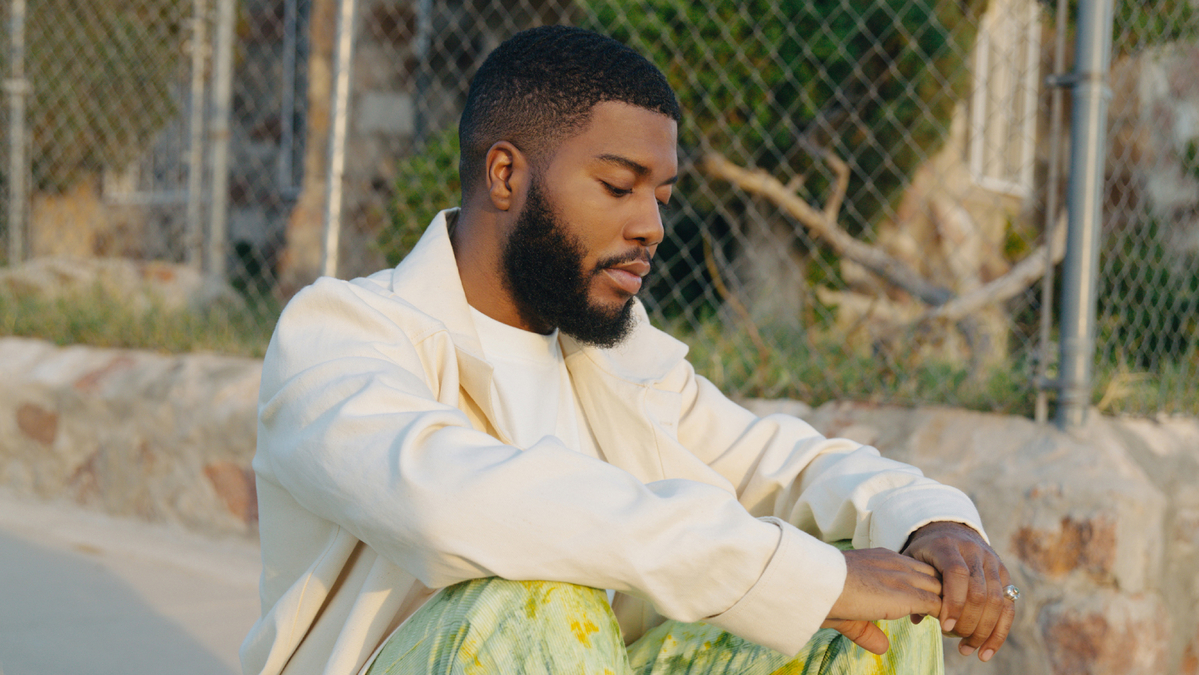 Khalid in white jacket sitting next to chain linked fence