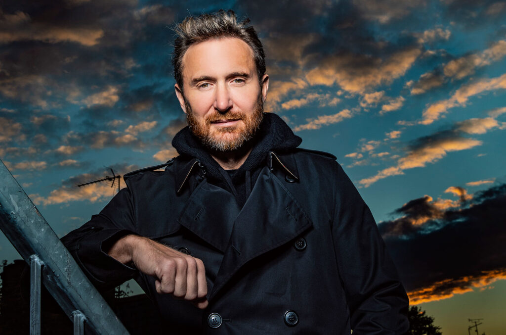 DJ David Guetta in Trench Coat with the sky and sundown behind him