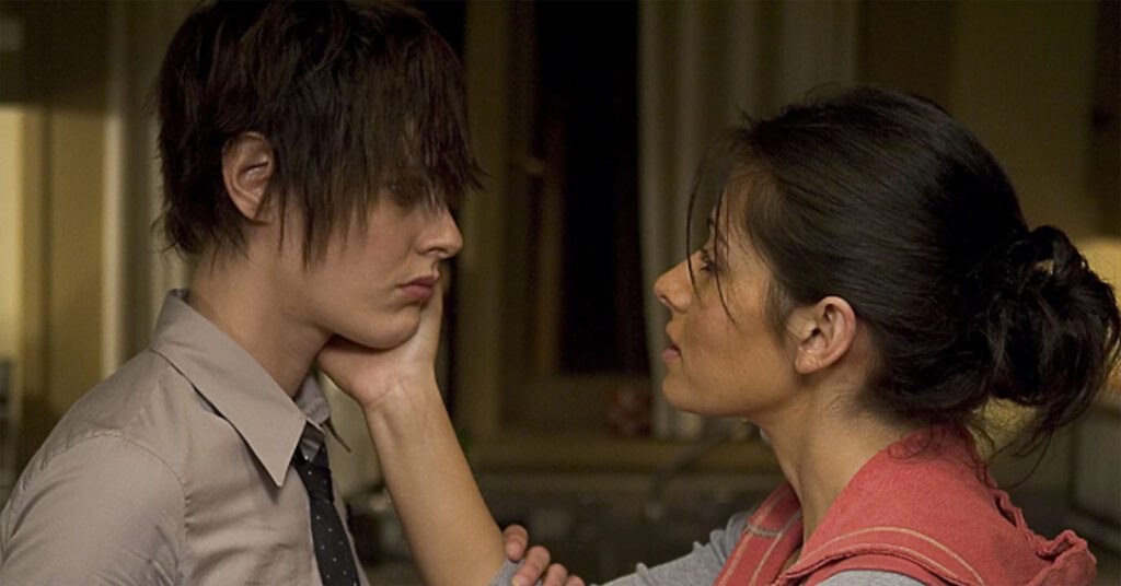 Carmen touching Shanes face and Shane with a short hair cut wearing a tie