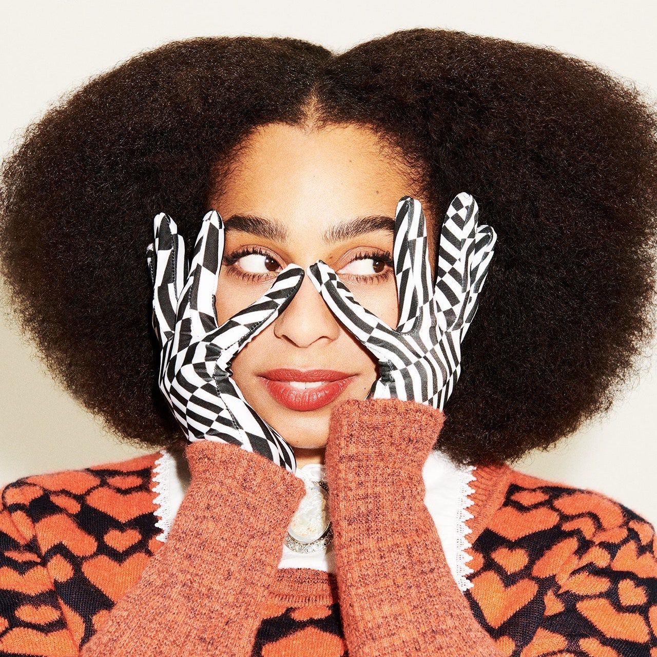 Celeste with graphic pattern gloves touching the sides of her face